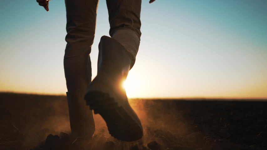 Agriculture. Farmer in rubber boots outdoors in field. Working agronomist walk on black earth soil. A man runs at sunset in a field. Farmer inspects fertile soil for the harvest. Agriculture concept