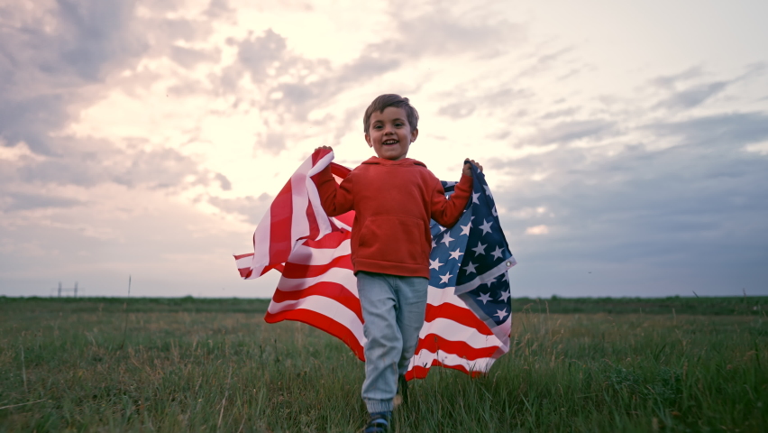 Cute little boy - American patriot kid running with national flag on open area field. USA, 4th of July - Independence day, celebration. US banner, memorial Veterans Day, election, America, labor.
