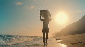 Rear view young long haired woman walks on sea sand and carries surfboard overhead walking through deserted seaside in search of good place to surf located on sunny evening beach. Active rest, extreme - Powered by Shutterstock - Get 15% off with code: PIKWIZARD15