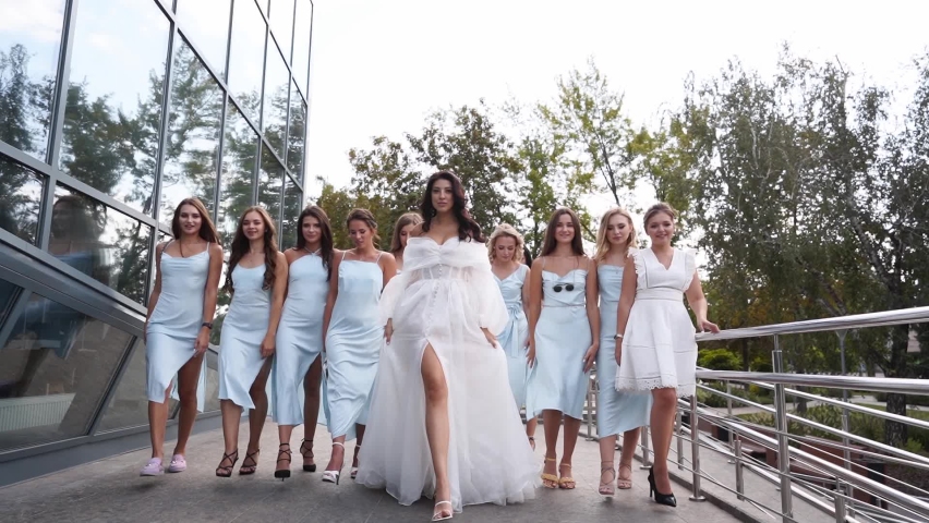 Beautiful bride, pretty bridemaids in pale blue dresses walk cheering waving hands. Woman with long airy bridal veil in elegant fluttering white dress partying flexing with girlfriends. Slow motion. | Shutterstock HD Video #1092267869