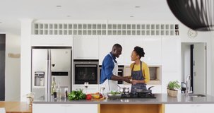 Video of happy african american couple dancing in kitchen. Love, relationship and spending quality time together concept.