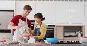 Video of happy diverse couple baking together in kitchen. Love, relationship and spending quality time together concept.