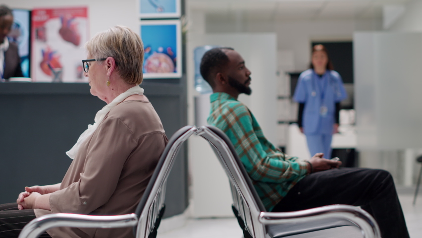 Medical assistant starting examination appointment with patient waiting in hospital reception lobby. African american man attending checkup visit with nurse and physician. Handheld shot. Royalty-Free Stock Footage #1092274175
