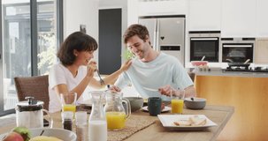 Video of happy diverse couple eating breakfast together in kitchen. Love, relationship and spending quality time together concept.