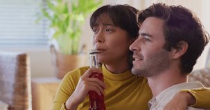 Video of happy diverse couple drinking beer and talking in living room. Love, relationship and spending quality time together concept.