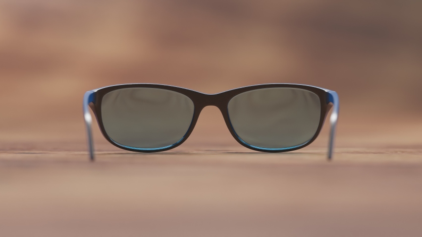 Pair of blue smart glasses laying on a wooden desk surface. AR overlay shows different functions like phone, messages, calendar, calculator, music, and shopping. Sophisticated piece of technology. Royalty-Free Stock Footage #1092277815