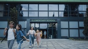 Diverse pupils leaving elementary school building. Happy children talking smiling walking outside. Group of cheerful energetic students with backpacks going out modern campus. Childhood concept. - Powered by Shutterstock - Get 15% off with code: PIKWIZARD15