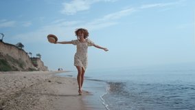 Happy cheerful girl jumping on water sandy beach summer day. Attractive curly woman running on ocean waves waving straw hat. Smiling cheerful lady have fun on seashore enjoy beautiful nature. - Powered by Shutterstock - Get 15% off with code: PIKWIZARD15