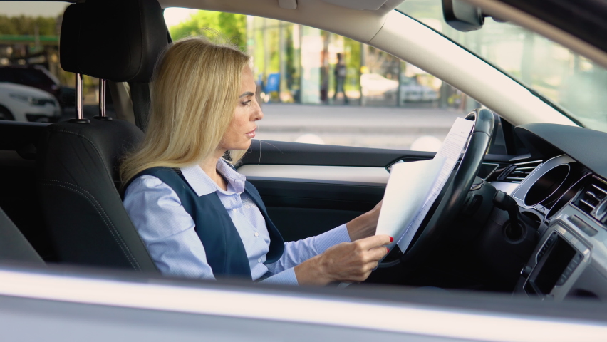 Portrait of a confident woman sitting in a car with documents in a business suit near a modern office building
