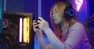 Asian woman gamer wearing gaming headphones holding joystick console to play video game and streaming online on computer PC neon light at home, tournament player E-Sport concept