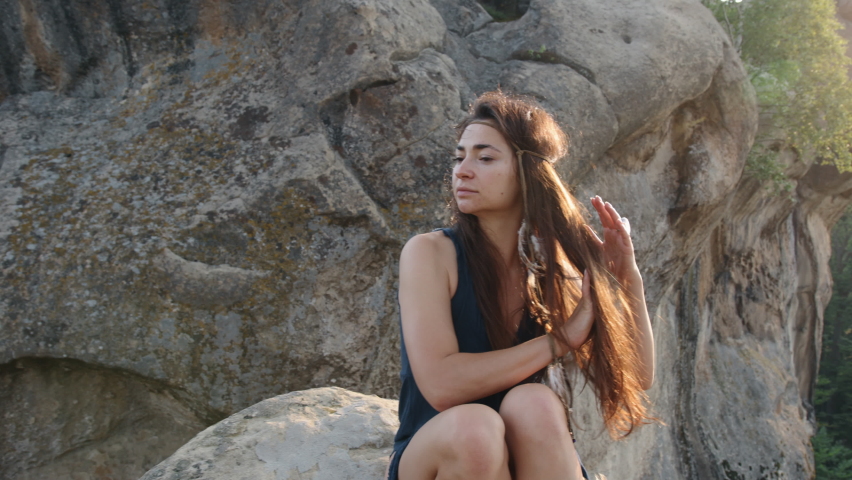 young woman relaxing outside in a blue silk dress sitting on rocky terrain with mountains in the background, relaxing in the outdoors as part of a travel lifestyle
