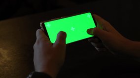 Man playing video game with green screen on smartphone at cafe. Mature man play smart phone, cell phone with green screen at table
