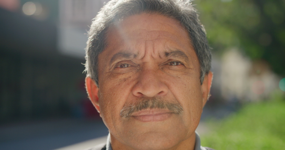 Closeup portrait of senior man standing in the street. Retired elderly latino gentleman looking straight at camera outside on a sunny day in summer. Face of honest and serious mature man in park Royalty-Free Stock Footage #1092296617