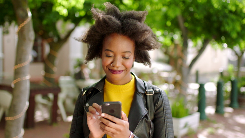 A black woman texting on social media using her phone outdoors in a park. Beautiful African female with an afro chatting on a dating app or replying to a text message. Lady reading news on cellphone Royalty-Free Stock Footage #1092296933