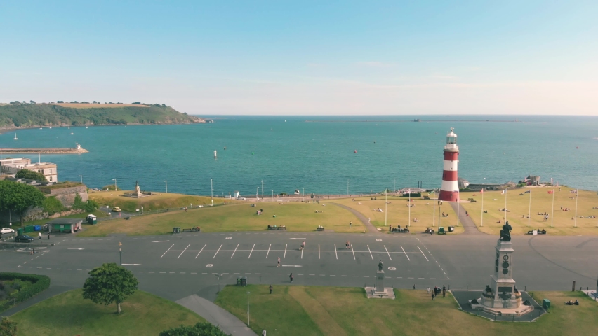 Aerial drone shot of a red and white striped lighthouse by the blue ocean in Plymouth, UK | Shutterstock HD Video #1092300927