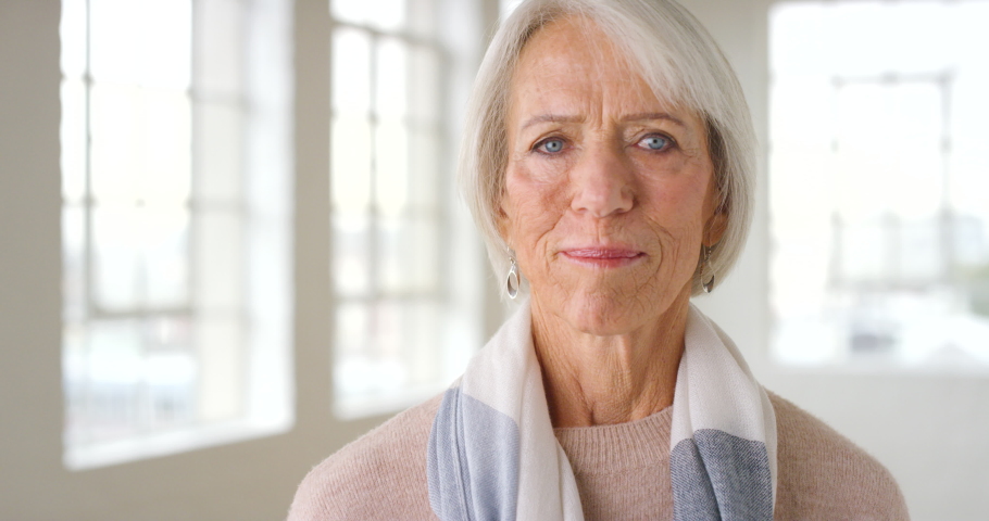 Portrait of a senior woman laughing inside a bright building with copy space. A beautiful and mature caucasian lady smiling with a joyful expression on her face while standing inside a modern room Royalty-Free Stock Footage #1092305263