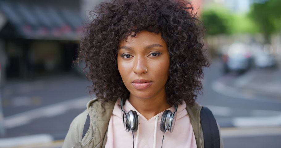 Portrait of a trendy young black woman with a carefree, cool and edgy attitude standing in the city. One beautiful, confident and serious african student with curly afro hair and headphones in town