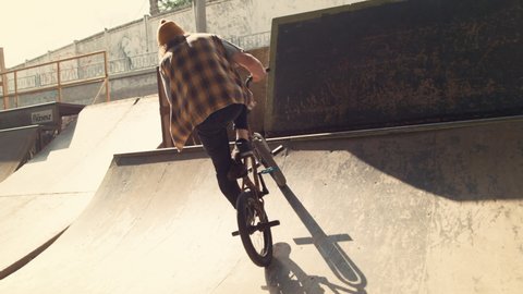 Sporty biker performing tricks on bmx bicycle in city skate park. Closeup unknown teenager rider jump high with bike outside. Extreme lifestyle of young man on bmx bike at urban space. Sport concept.