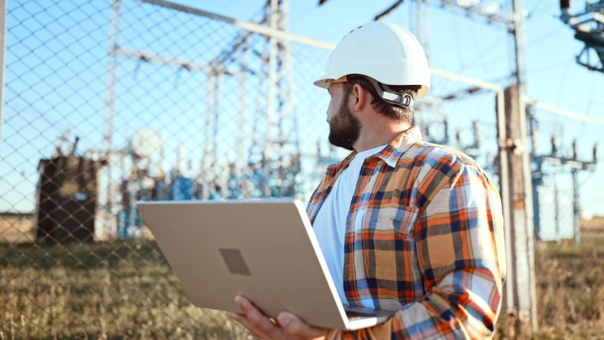 Design engineer in helmet holds laptop in hands at construction site in field, estimating investment attractiveness this object. Male compares his project with customer project. Using technologies. | Shutterstock HD Video #1092309105