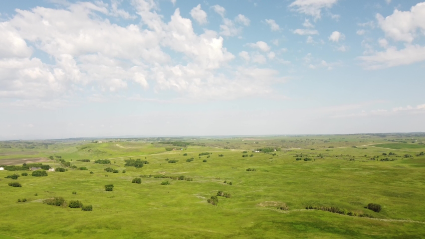 High aerial tilt down shot of rolling hills and ranching farms on the Alberta Prairies.