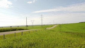 Tracking motion of adventure motorcycle riders travelling fast down a county gravel road with Transmission towers and power poles on the Canadian Prairies.
