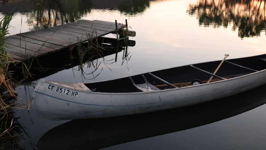 A metal canoe floats next to an old wooden dock at sunrise on a small pond in Dayton, Nevada.  Shallow Depth of Field.