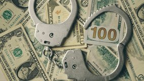 Close up of rotation metal handcuffs over stack of dollar banknotes. Dirty money. Concept of financial crimes or bribery and cash corruption police and deputies or fraud. 4k footage - Powered by Shutterstock - Get 15% off with code: PIKWIZARD15