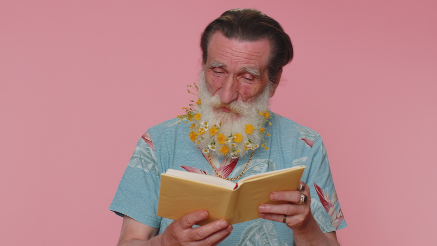 Senior man with flowers in gray-haired beard reading funny interesting fairytale story book, leisure hobby, knowledge wisdom, education, learning, study, wow. Elderly grandfather on pink background | Shutterstock HD Video #1092320829