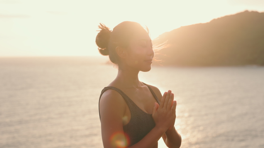 Silhouette of Asian woman improves balance for body, mind and spirit with yoga practice at sunset on the beach. Slow movements and deep breathing improves strength and flexibility. mental health | Shutterstock HD Video #1092326015
