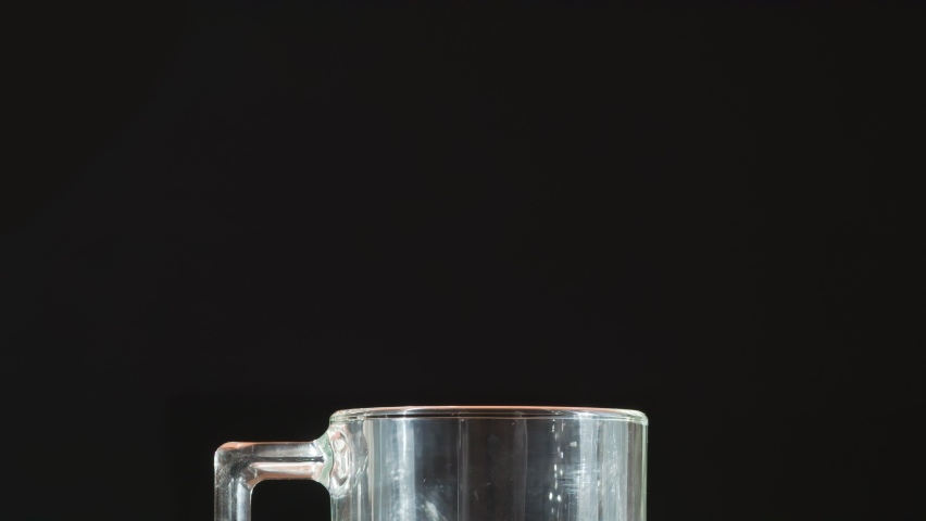 Boiling Water Jet for Tea. A jet of boiling water falls into a glass tea mug, creating puffs of white steam against a black background Royalty-Free Stock Footage #1092326551