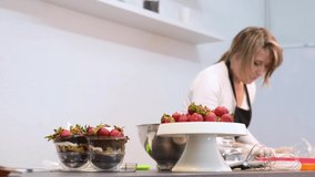 A woman cook in a white kitchen prepares a chocolate dessert with strawberries. Slow motion video