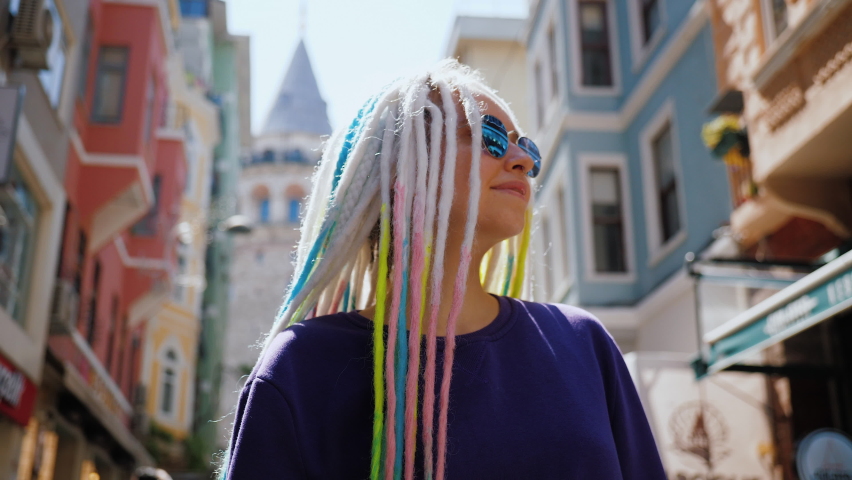 Portrait of smiling European woman with sunglasses and dreadlocks walking street against Galata Tower. Emotions of joy and happiness. Attractive hipster tourist