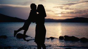 A slow motion video of a mother spinning her son in her arms by the sea at sunset. Happy family having fun together on the ocean beach on vacation. - Powered by Shutterstock - Get 15% off with code: PIKWIZARD15