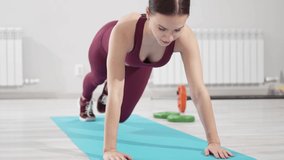 a beautiful and slender woman in a burgundy tracksuit exercises on a mat in a gym. video and online lessons for fitness. clothes and shoes for gymnastics. professional trainer. 