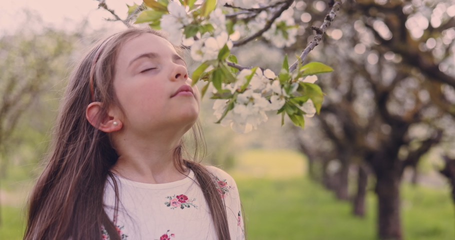 Girl smelling the  aroma of blooming spring trees in apple orchard. Bulgarian woman in folklore dress in garden