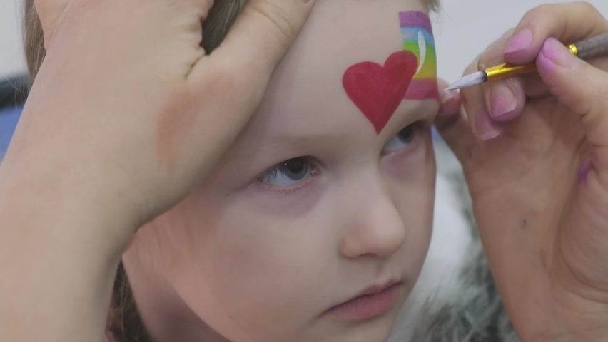 Artist painting a rainbow and heart on girl