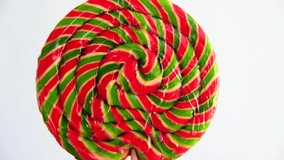 Striped fruit green and red lollipop rotates on blue background. 4K resolution real time video. Close-up view. Selective focus. Confectionery theme.