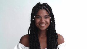 Isolated portrait against a white wall background of a young multiethnic woman with stylish dreadlocks looking at the camera and breaking into a beautiful healthy white toothy smile. Copy ad space