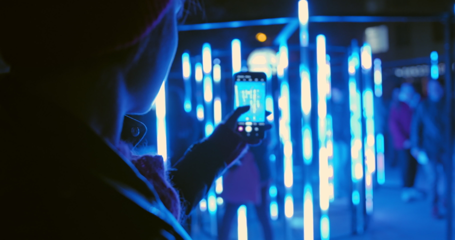 Young female recording video of neon lights performance show at night with smartphone. Photography, video, lights entertainment and technology concept