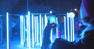Beautiful woman recording video of neon lights performance show at night with smartphone. Photography, video, lights entertainment and technology concept