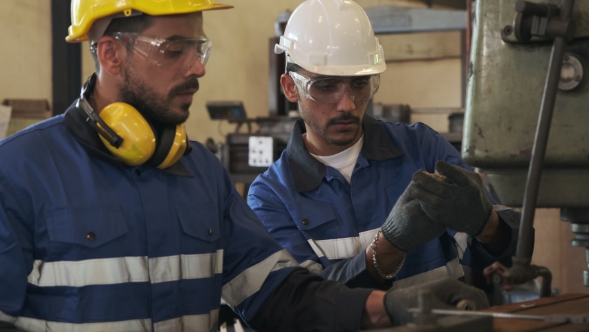 Two caucasian industrial workers using vernier caliper measures workpiece to verify its clearance in factory.