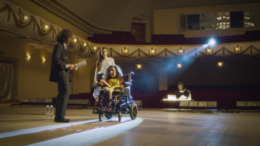 Actress with a disability driving around the stage in an electric wheelchair and rehearsing a performance with actors and a director in a dim theater, with a spotlight Royalty-Free Stock Footage #1092362857
