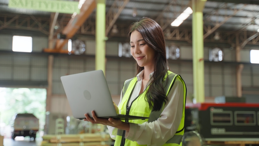 Portrait of Asian female industry worker working in factory warehouse. Attractive women industrial engineer processes orders and products alone at manufacturing plant then looking at camera with smile