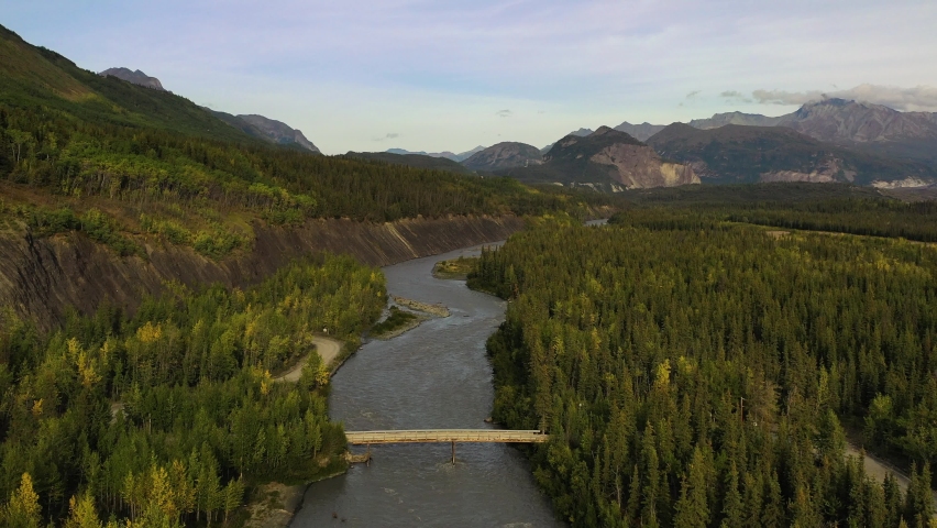 Aerial flyover following Sag river stream surrounded with forests and high mountains in Deadhorse, Alaska