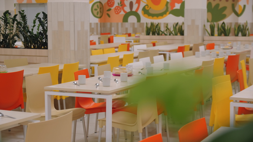 Long served tables with colorful plastic chairs for students in spacious school canteen. Modern catering service Royalty-Free Stock Footage #1092367333