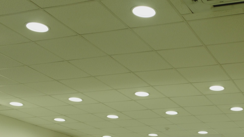 Many Circle Led lamps built into the ceiling glowing in the dark . To include and switch off . White rounded lights turns on alternately on ceiling of dark, industrial room. Lighting equipment concept Royalty-Free Stock Footage #1092370959