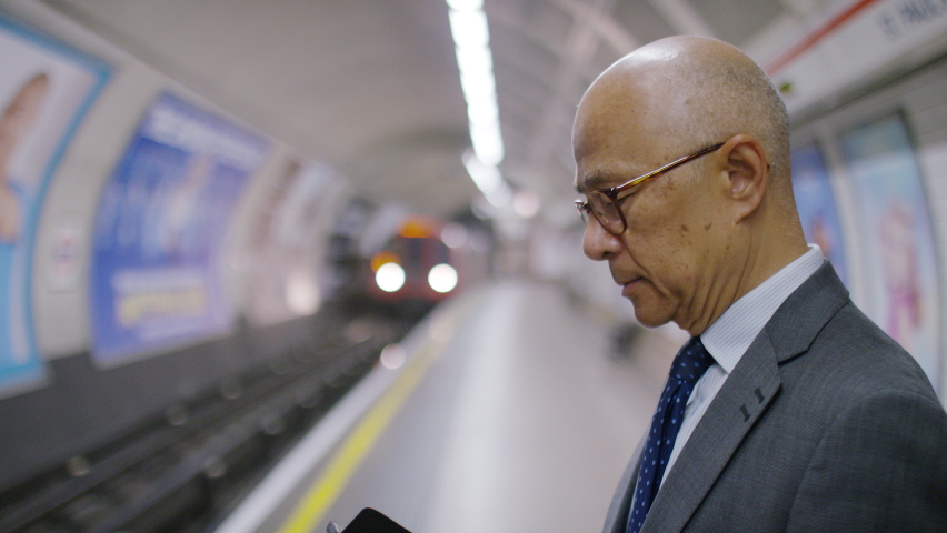 Senior Asian male reading his phone as a subway train approaches, in slow motion