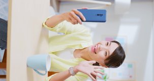 vertical of Asian woman sitting on chair using smartphone has video call with friends or family feeling happy smiling when relax in living room at home