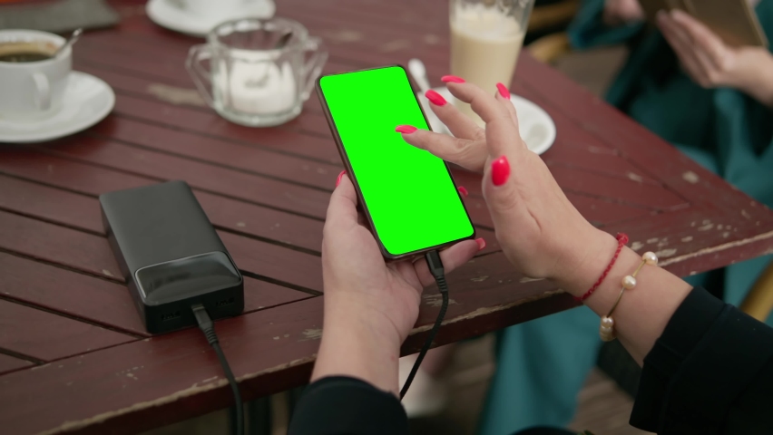 a woman close-up looks at the screen of a smartphone connected to an external battery, power bank. Close-up of a phone green screen.
