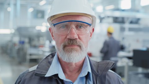 Close Up Portrait of a Senior, Successful Male Engineer in White Hard Hat and Safety Glasses, Standing at Electronics Manufacturing Factory. Heavy Industry Professional Posing for Camera.